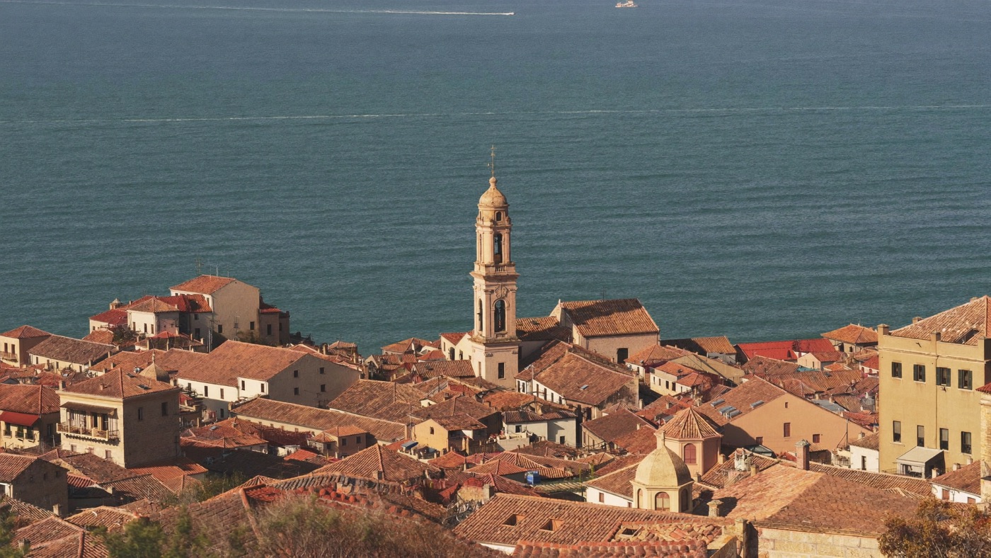 Terracotta rooftops of a Spanish coastal town above a deep blue bay